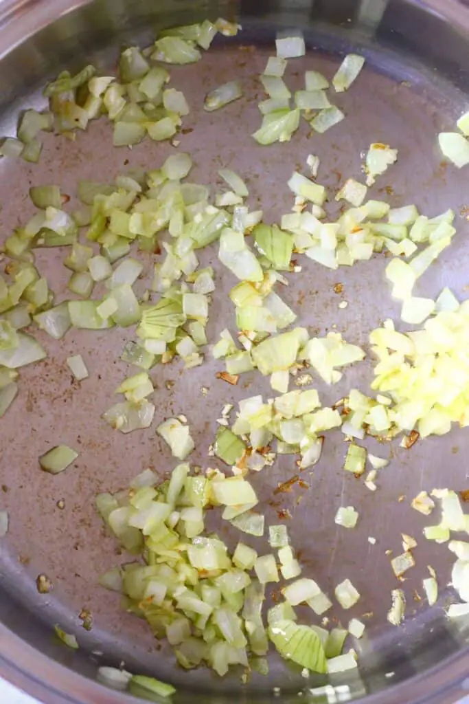 Diced onions being fried in a silver saucepan