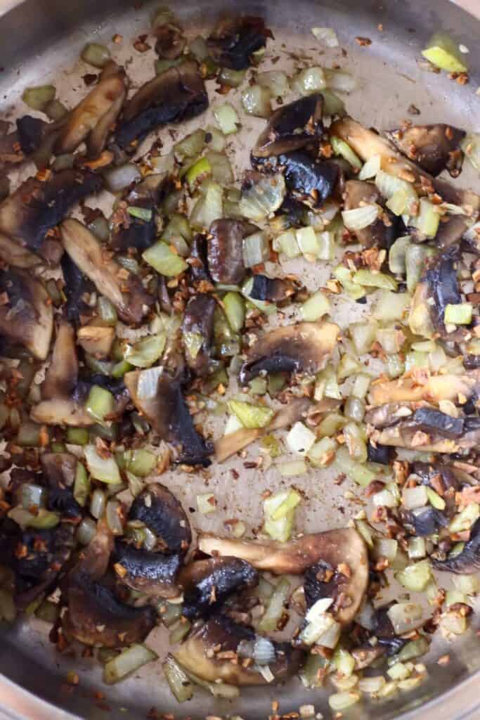 Diced onions and sliced mushrooms being fried in a silver saucepan