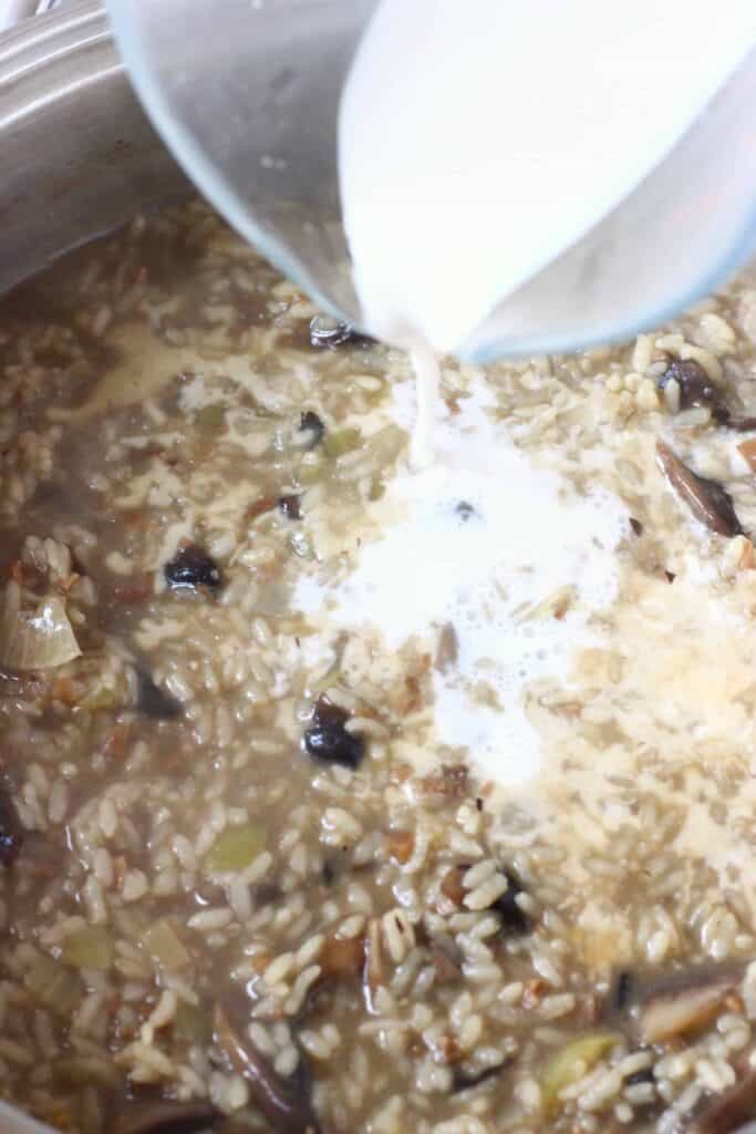 Sliced mushrooms and rice in a pan with a jug pouring milk into it