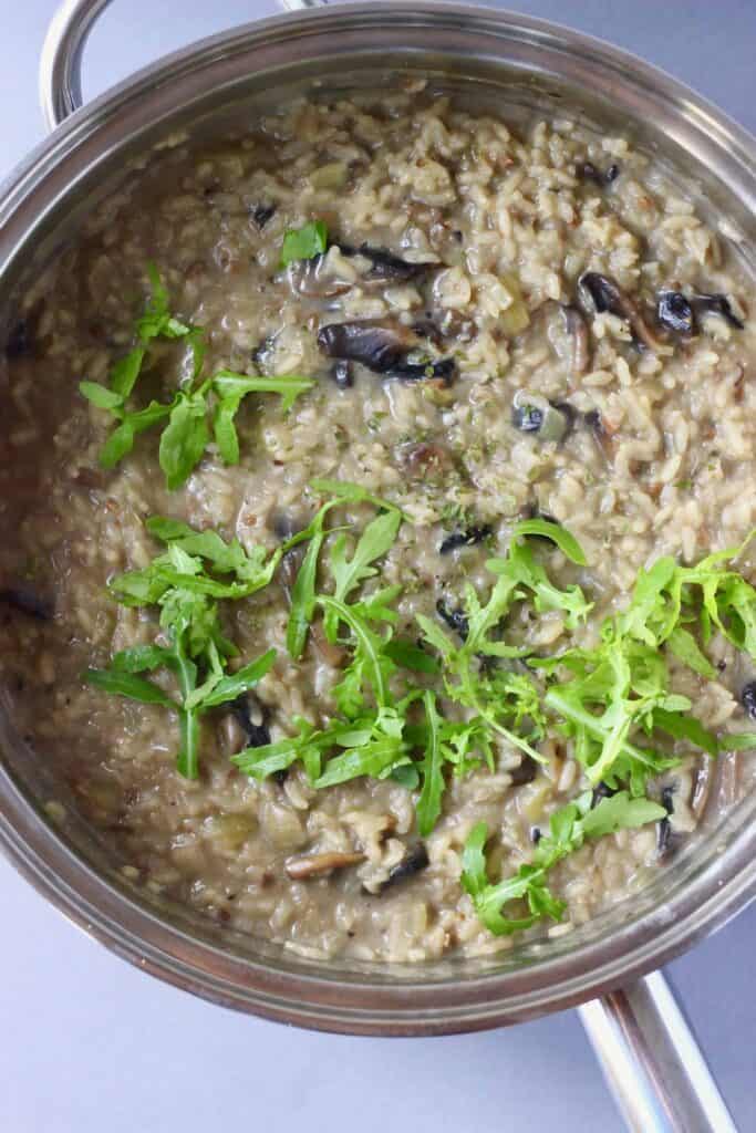 Mushroom risotto topped with rocket in a silver pan against a grey background