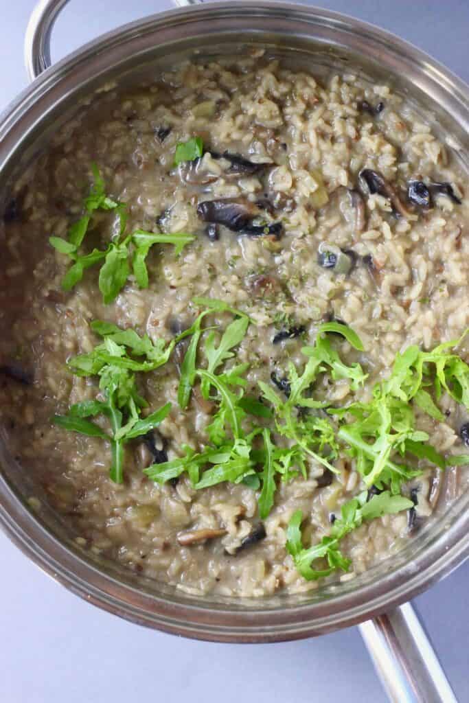Mushroom risotto topped with rocket in a silver pan against a grey background