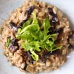 A pile of mushroom risotto topped with rocket on a light blue plate