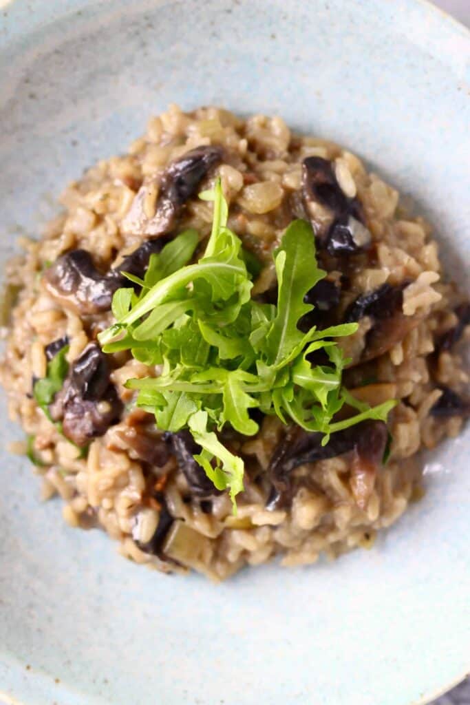 A pile of mushroom risotto topped with rocket on a light blue plate