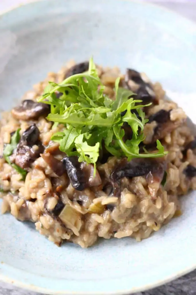 A pile of mushroom risotto topped with rocket on a light blue plate