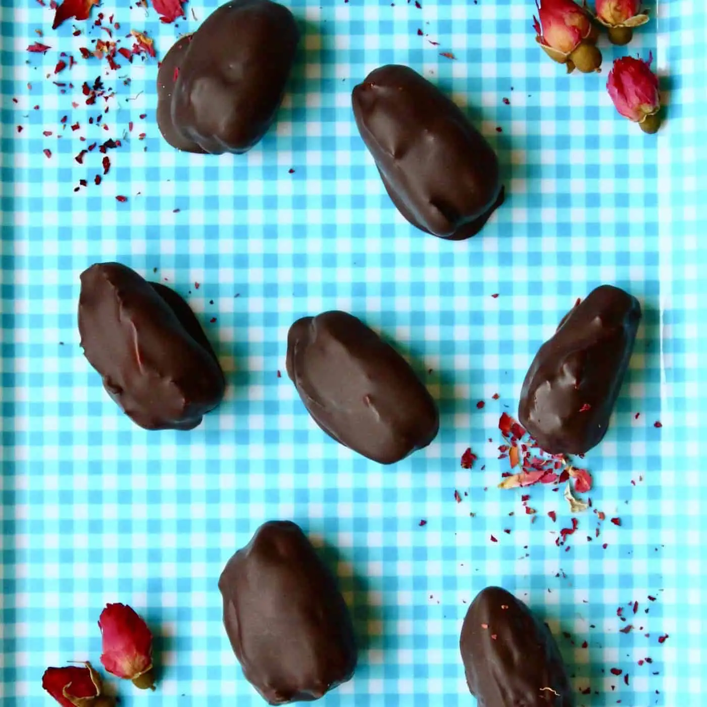 Seven chocolate-covered dates against a blue checked background