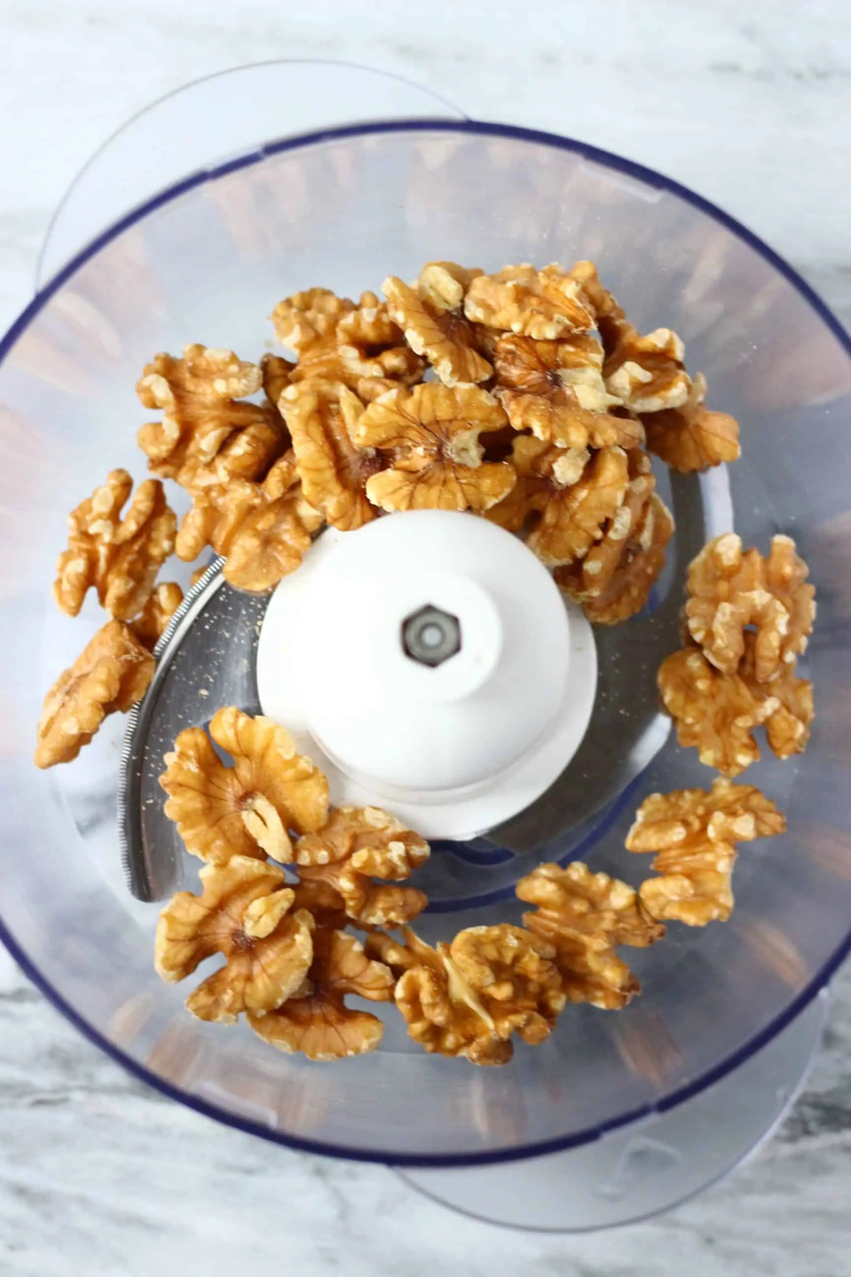 Walnuts in a food processor against a marble background