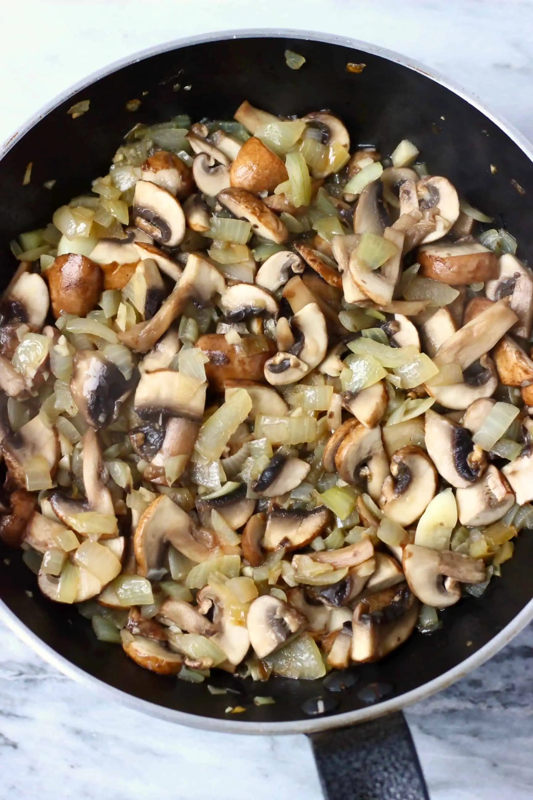 Diced onion, minced garlic and sliced mushrooms being fried in a frying pan 