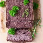 A black bean vegan meatloaf decorated with herbs with two slices next to it