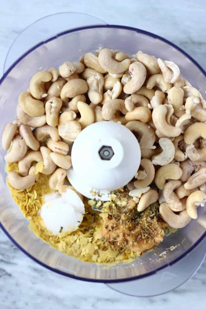Cashew nuts, coconut oil, miso and nutritional yeast in a food processor against a marble background