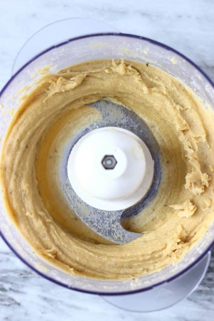 Yellow cashew paste in a food processor against a marble background