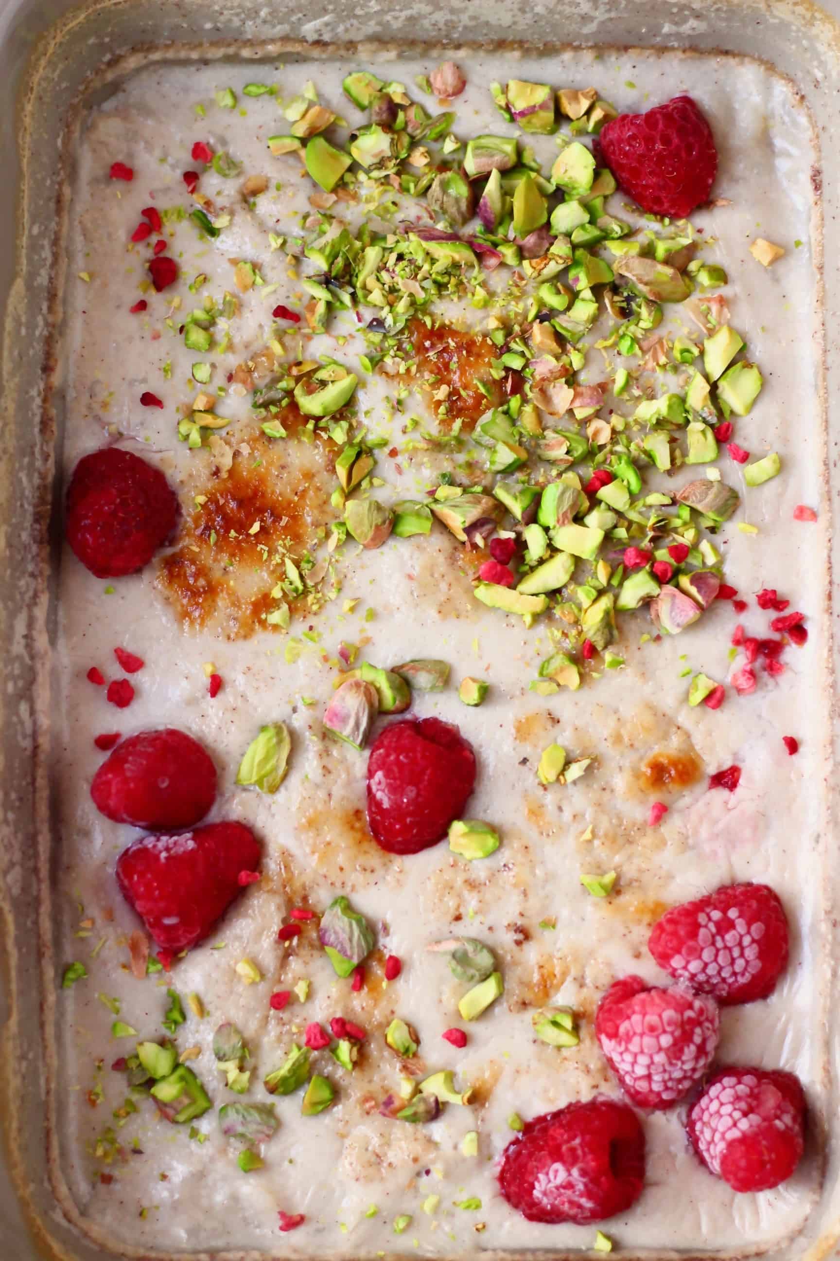 Vegan rice pudding in a grey rectangular baking dish topped with chopped pistachios and fresh raspberries