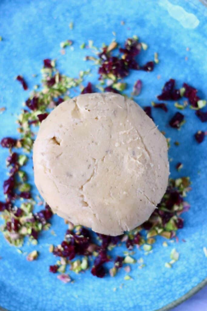 A ball of cashew cheese on a blue plate scattered with chopped pistachios and dried cranberries 