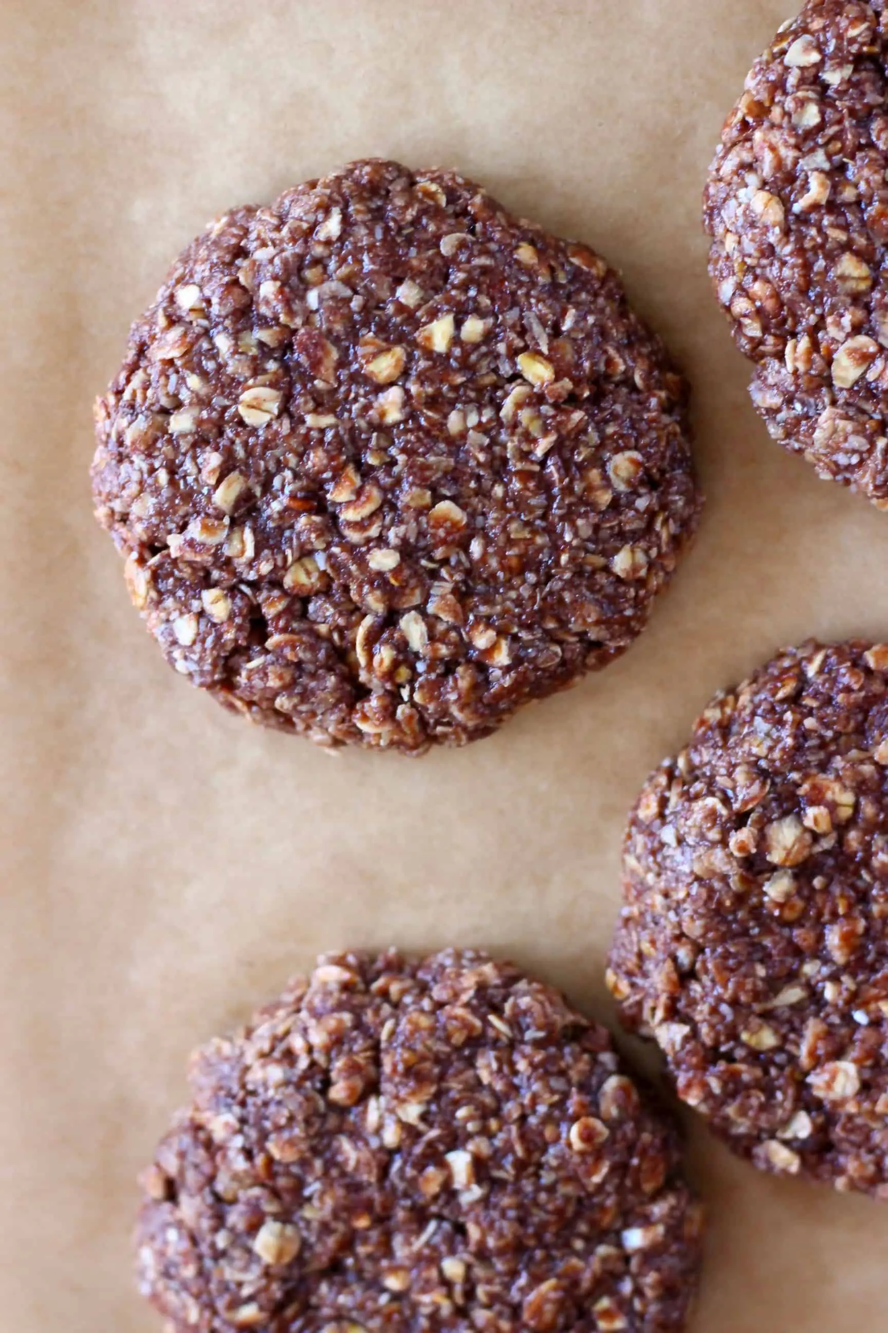 Four raw chocolate oatmeal cookies on a sheet of brown baking paper