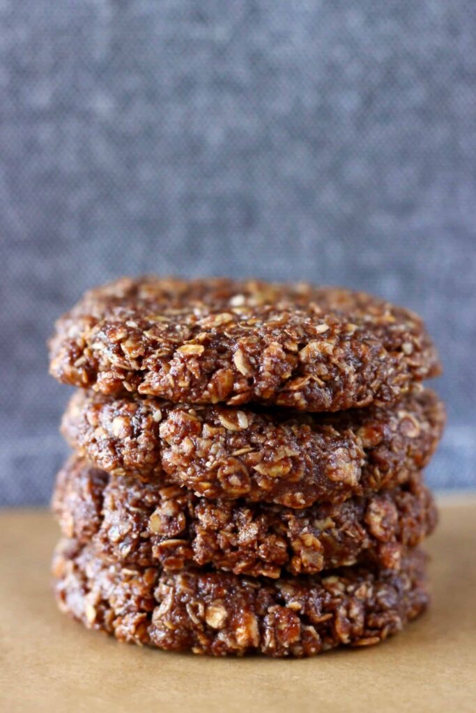 Four raw chocolate oatmeal cookies stacked on top of each other on a sheet of brown baking paper against a grey background