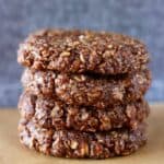 Four gluten-free vegan chocolate no-bake cookies stacked on top of each other on a sheet of baking paper