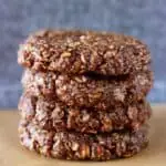 Four gluten-free vegan chocolate no-bake cookies stacked on top of each other on a sheet of baking paper