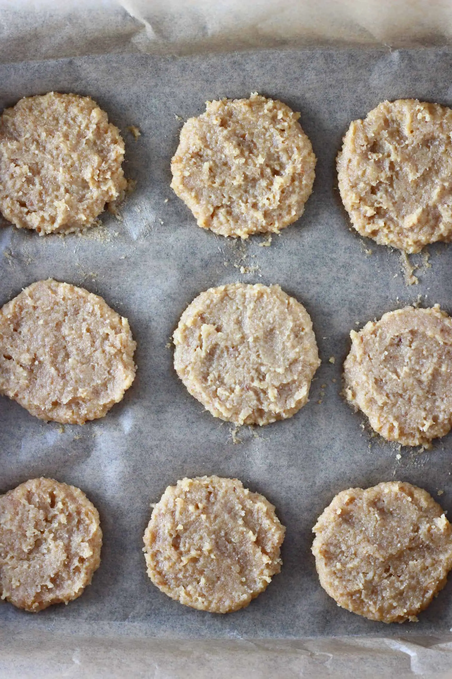Nine raw almond butter cookies on a baking tray lined with baking paper