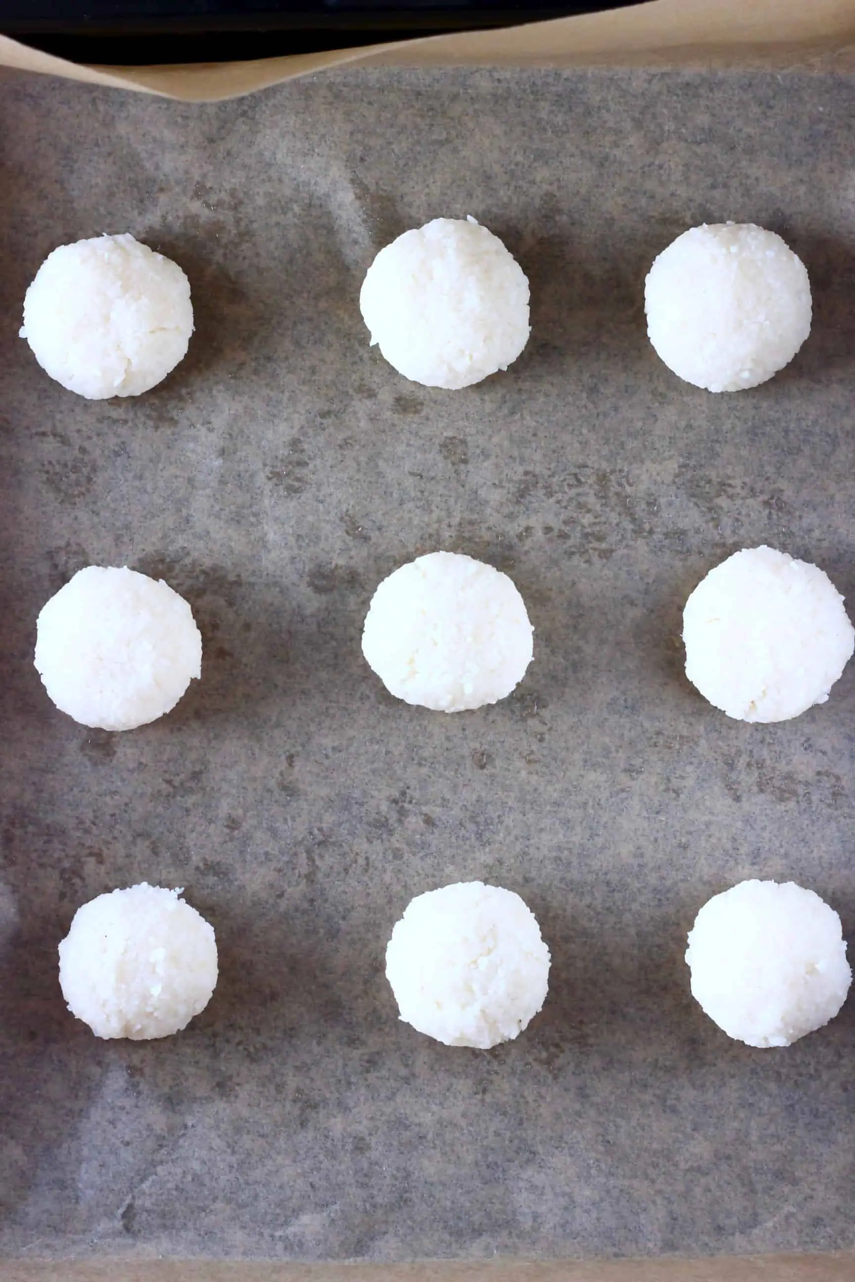 Nine raw vegan macaroons on a baking tray covered in brown baking paper