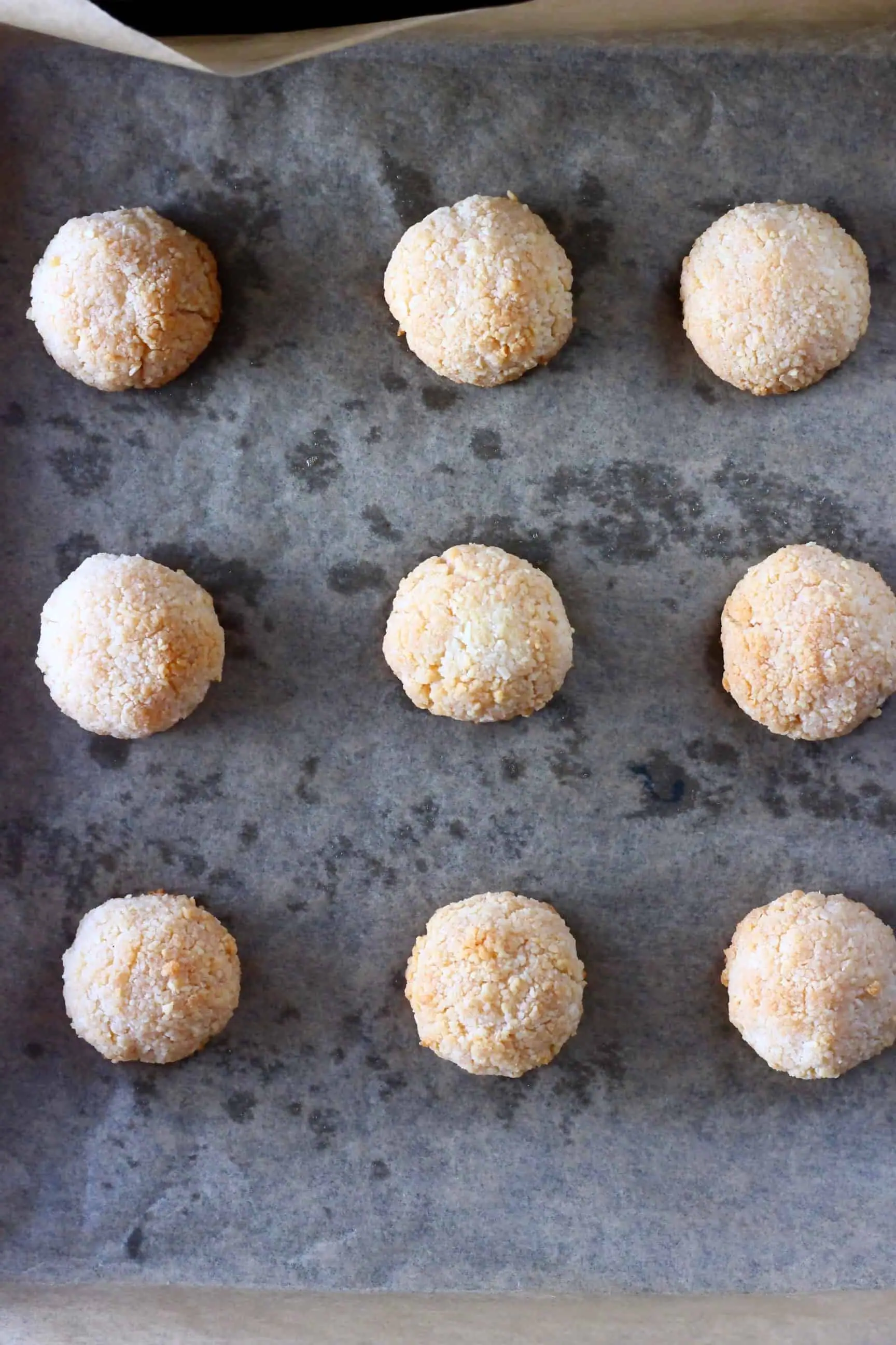 Nine vegan macaroons on a baking tray covered in brown baking paper