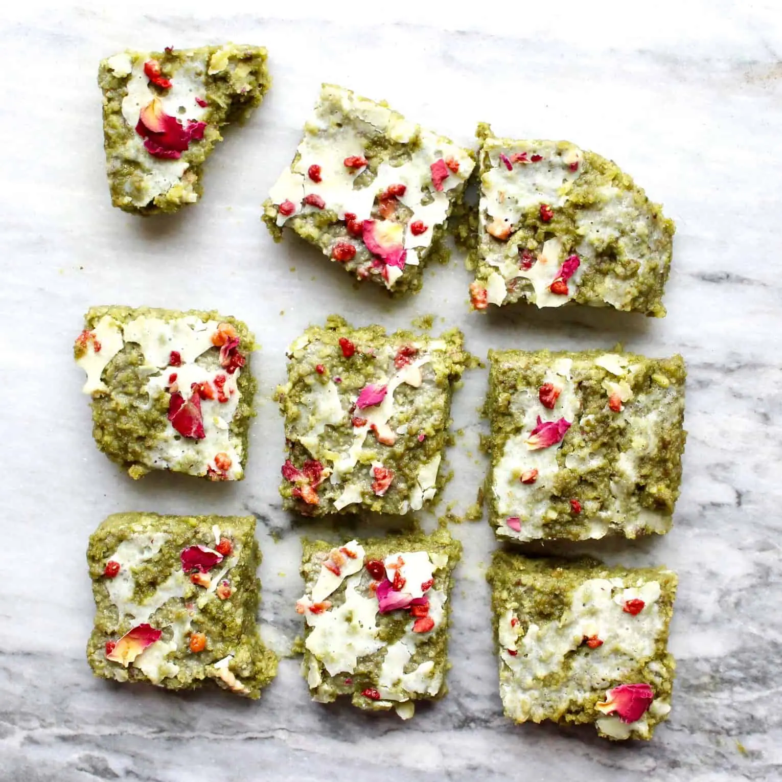 Photo of nine green brownies drizzled with white chocolate and decorated with rose petals on a marble background