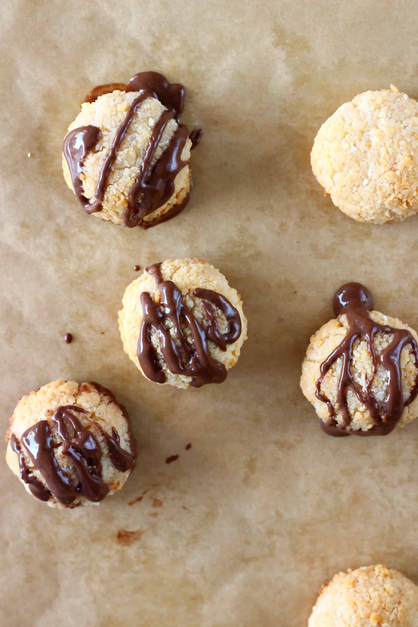 Six vegan macaroons drizzled with melted chocolate on a sheet of brown baking paper