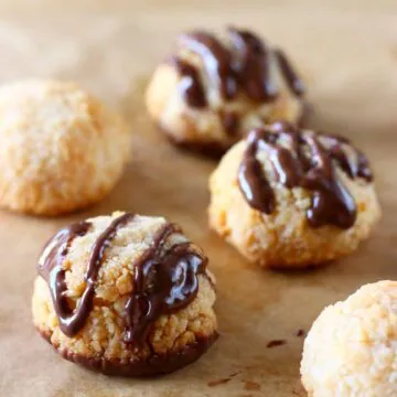 Five vegan coconut macaroons drizzled with melted chocolate on a sheet of brown baking paper