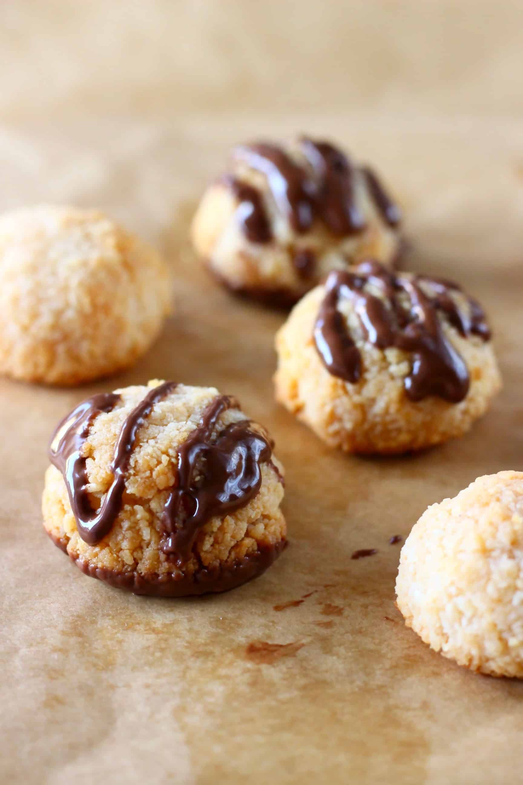 Five vegan macaroons drizzled with melted chocolate on a sheet of brown baking paper