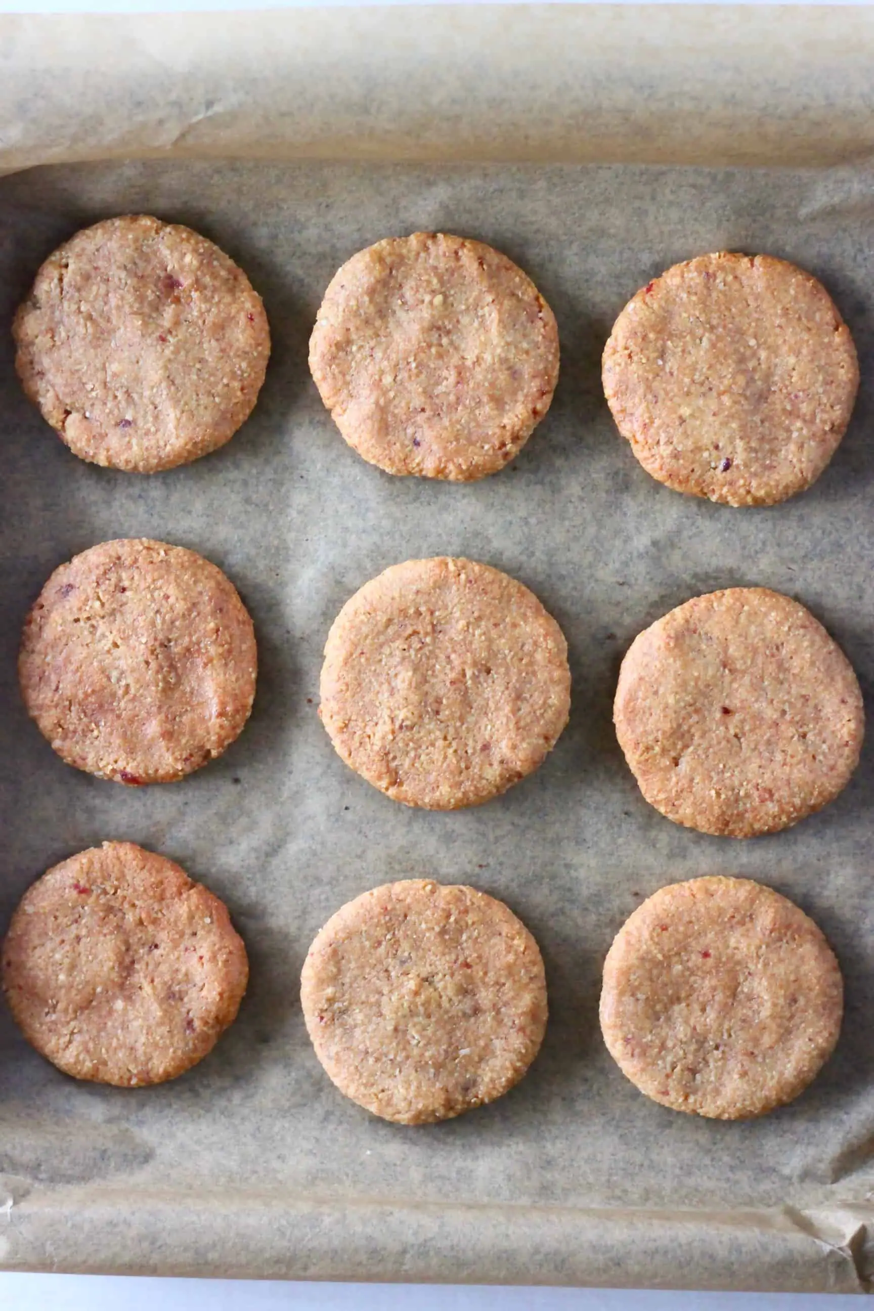 Nine almond butter cookies on a sheet of brown baking paper