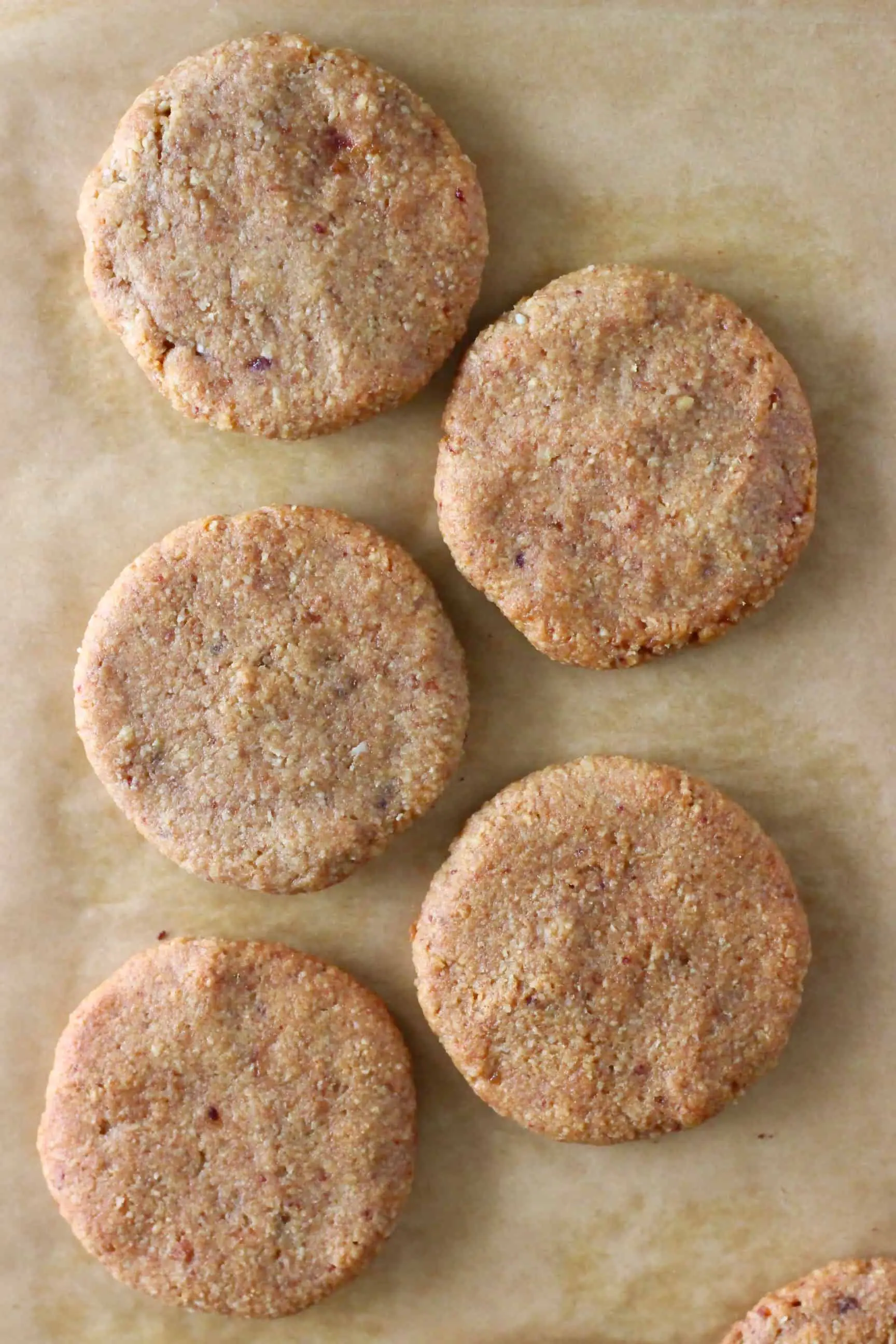 Five almond butter cookies on a sheet of brown baking paper