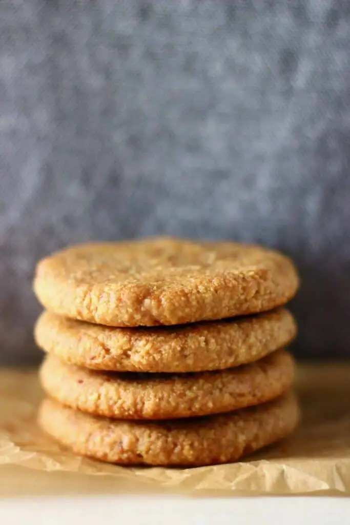 Four golden brown cookies stacked on top of each other on a sheet of brown baking paper against a grey background