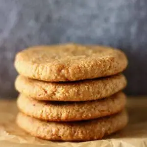 Four almond butter cookies stacked on top of each other on a sheet of baking paper
