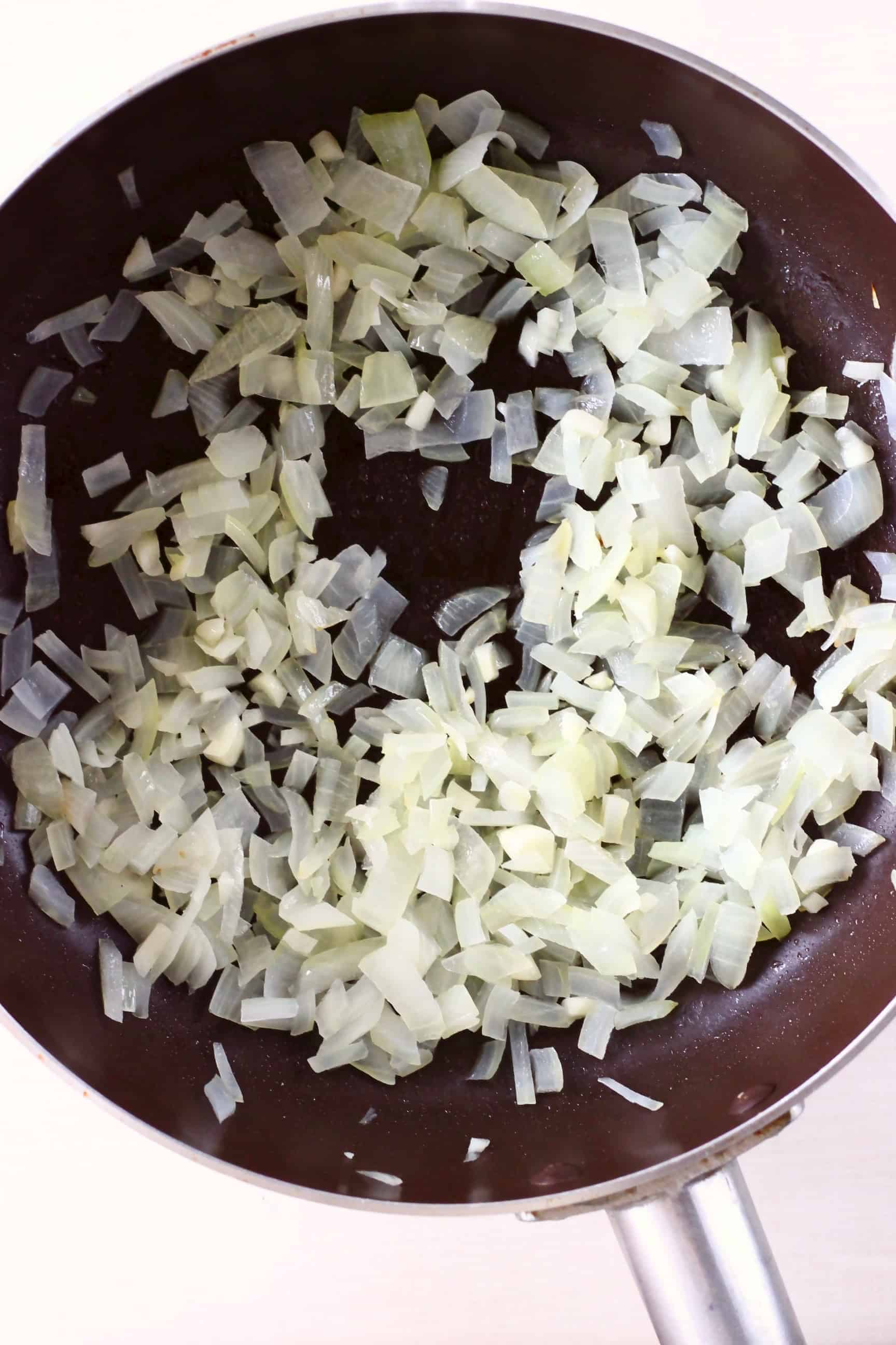 Diced onion being fried in a black frying pan against a white background