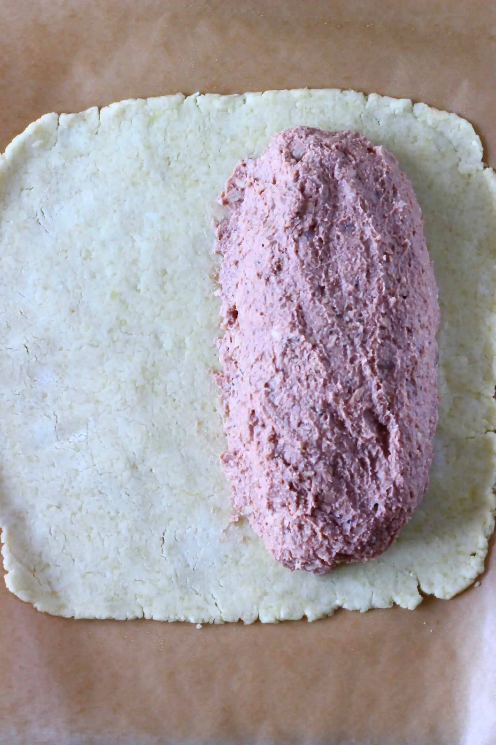 A square of raw gluten-free vegan pastry dough with a sausage-shaped raw vegan wellington filling on top of it 