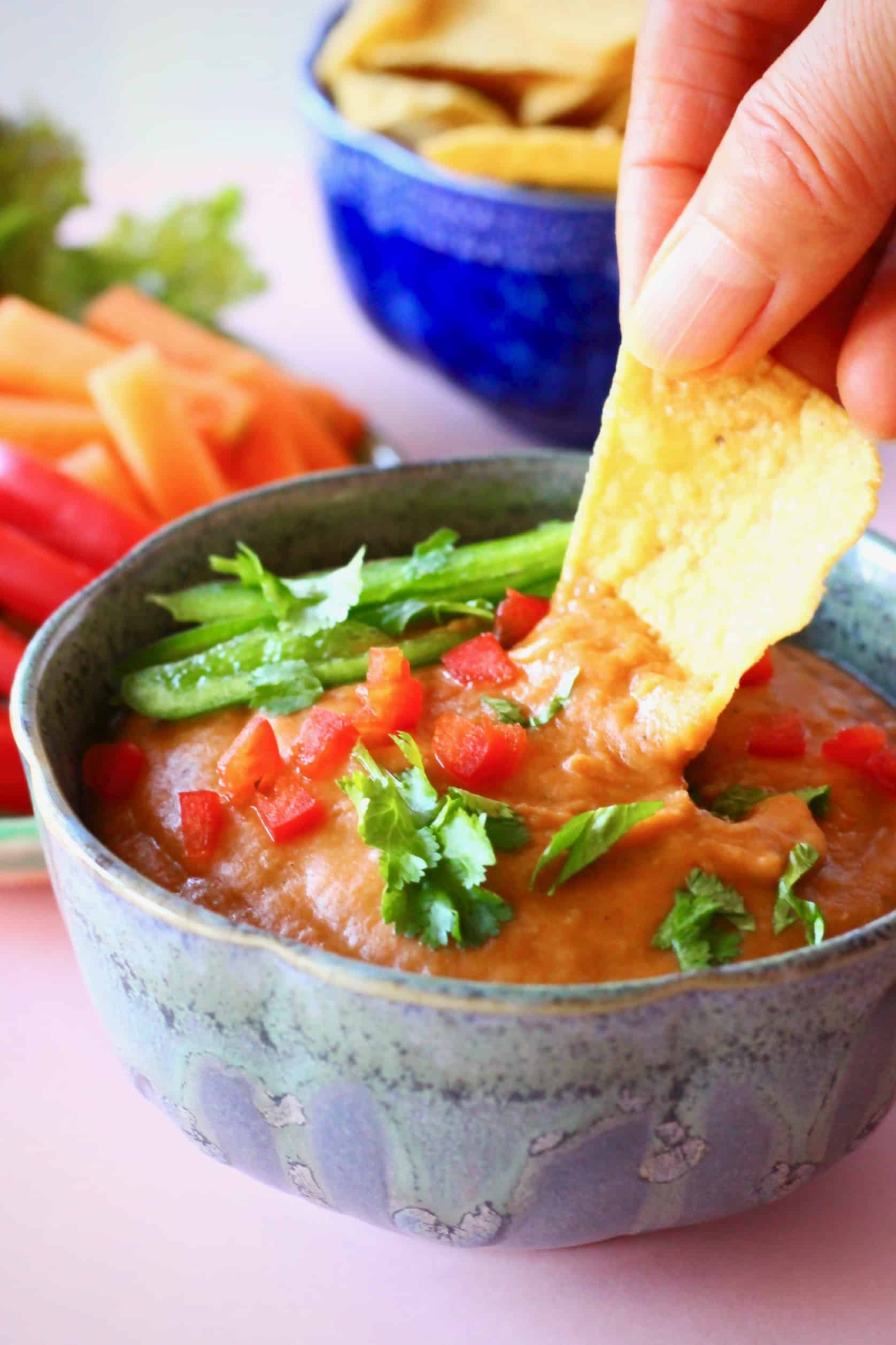 Photo of orange cheese sauce in a grey bowl with a hand dipping a tortilla chip into it