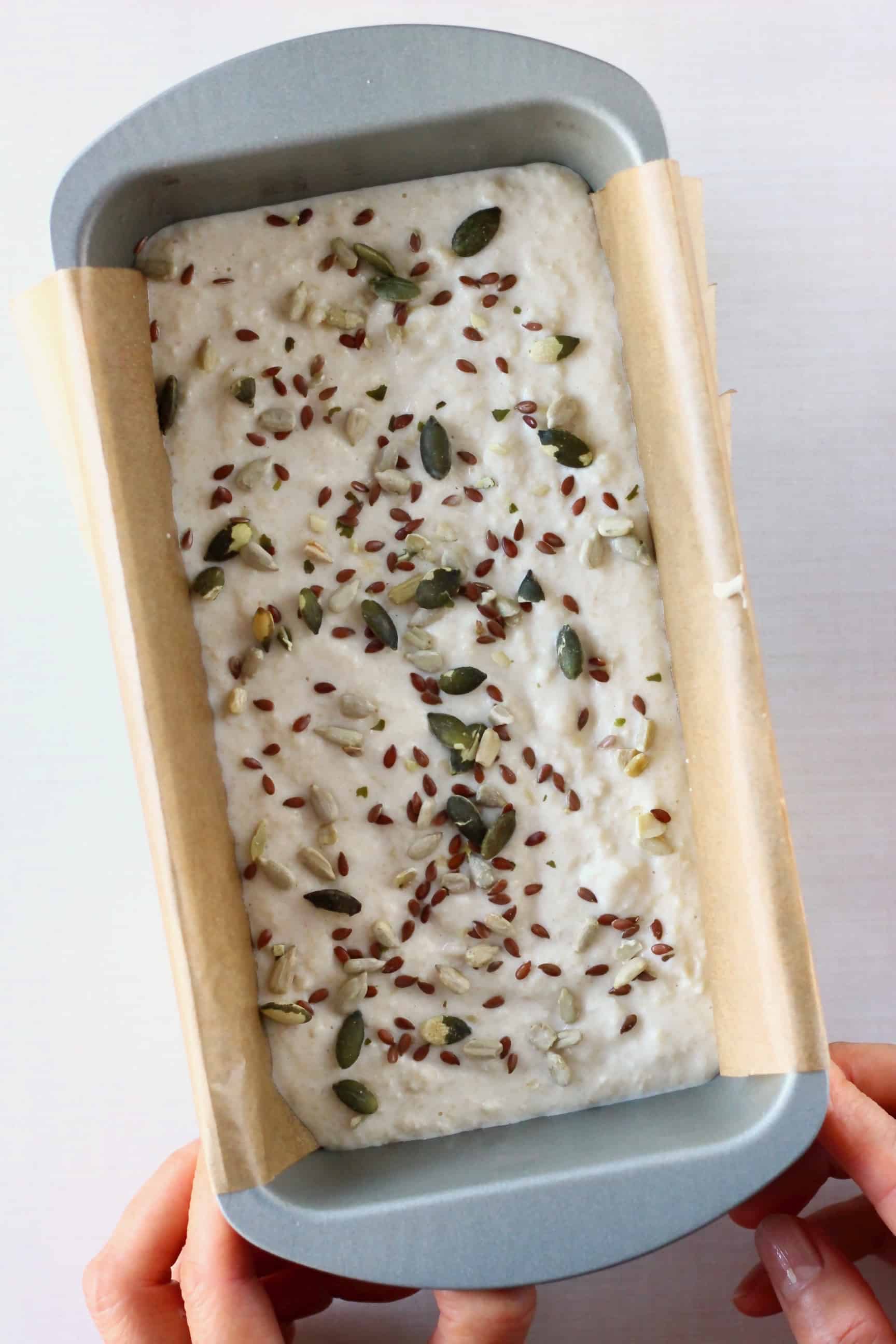 Gluten-free vegan almond bread batter sprinkled with mixed seeds in a loaf tin lined with brown baking paper 