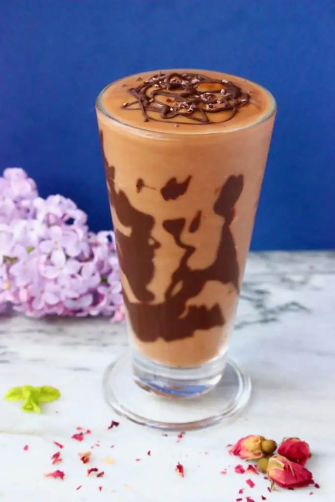 Chocolate milkshake with chocolate on the sides in a tall glass on a marble surface against a dark blue background