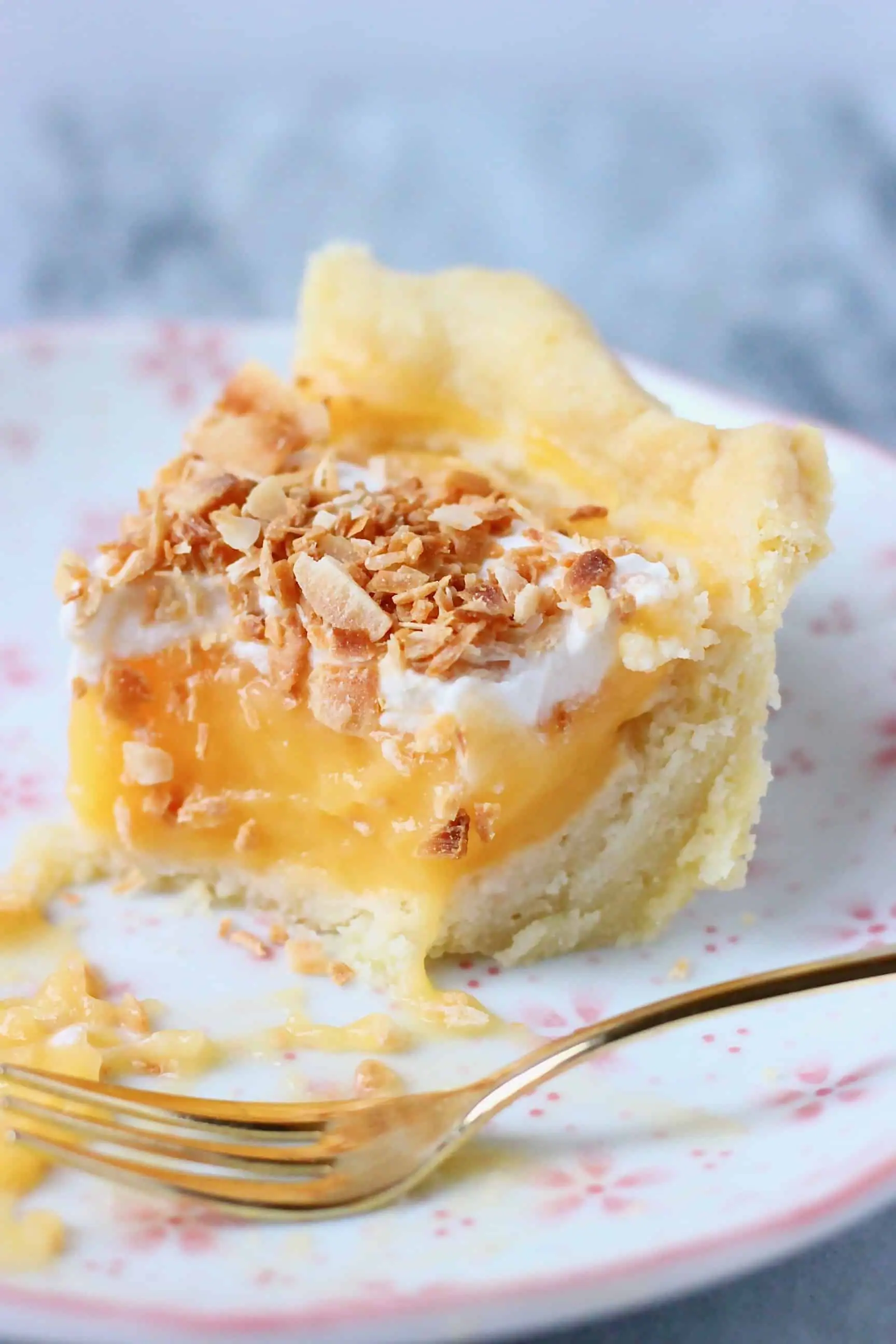 A slice of pie filled with lemon curd topped with cream and toasted coconut on a plate