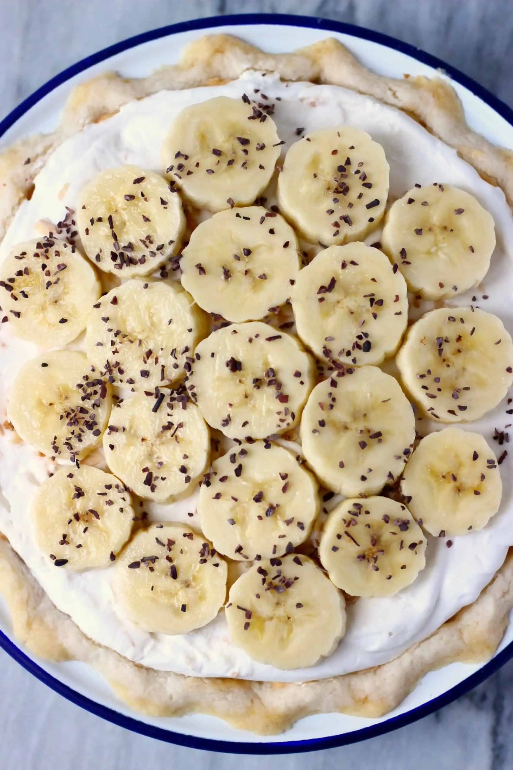 A pie crust filled with white cream and topped with banana slices and cacao nibs in a pie dish 