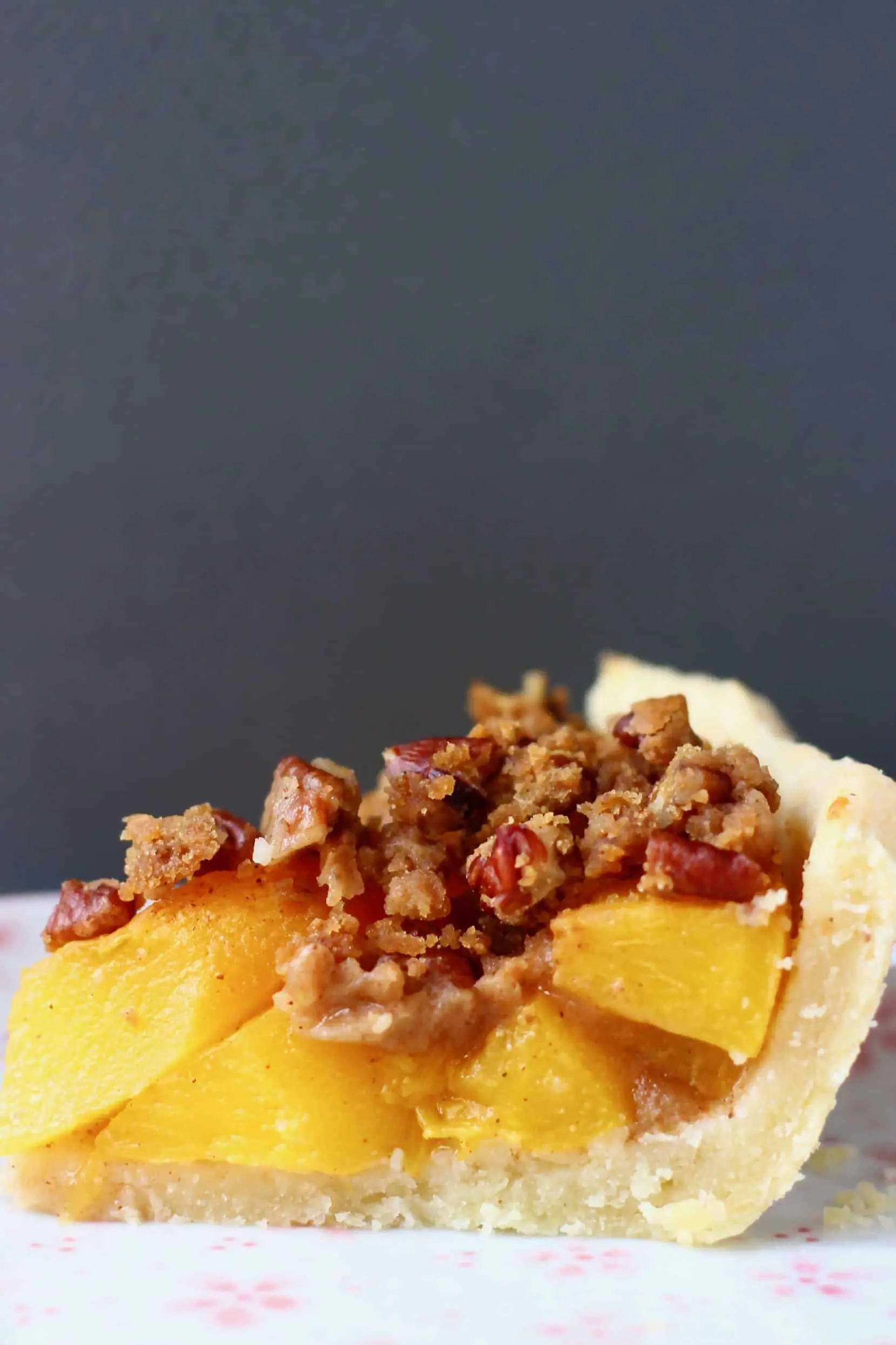 A slice of peach pie topped with brown crumble topping on a white plate