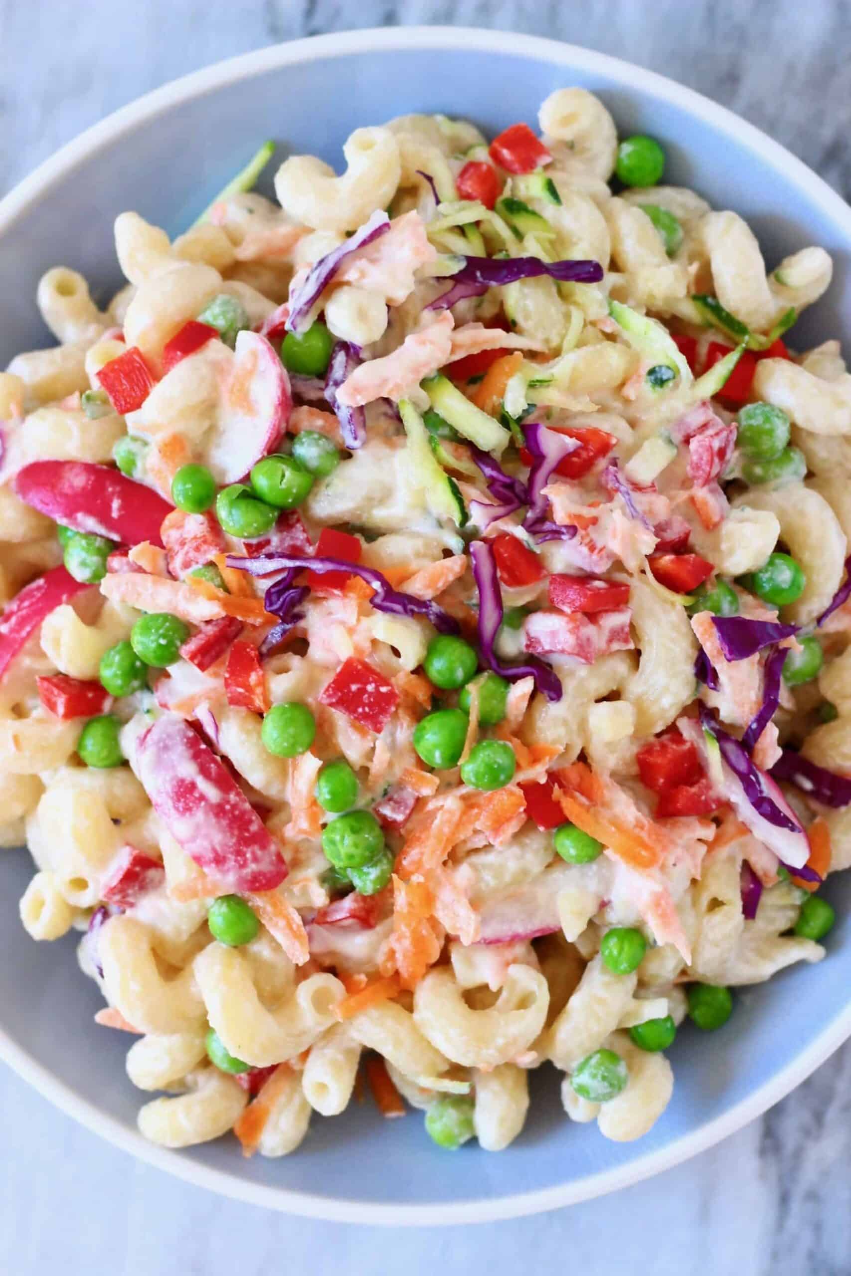 Pasta salad with green peas, shredded cabbage, radish and carrots in a mayonnaise dressing in a light blue bowl against a marble background