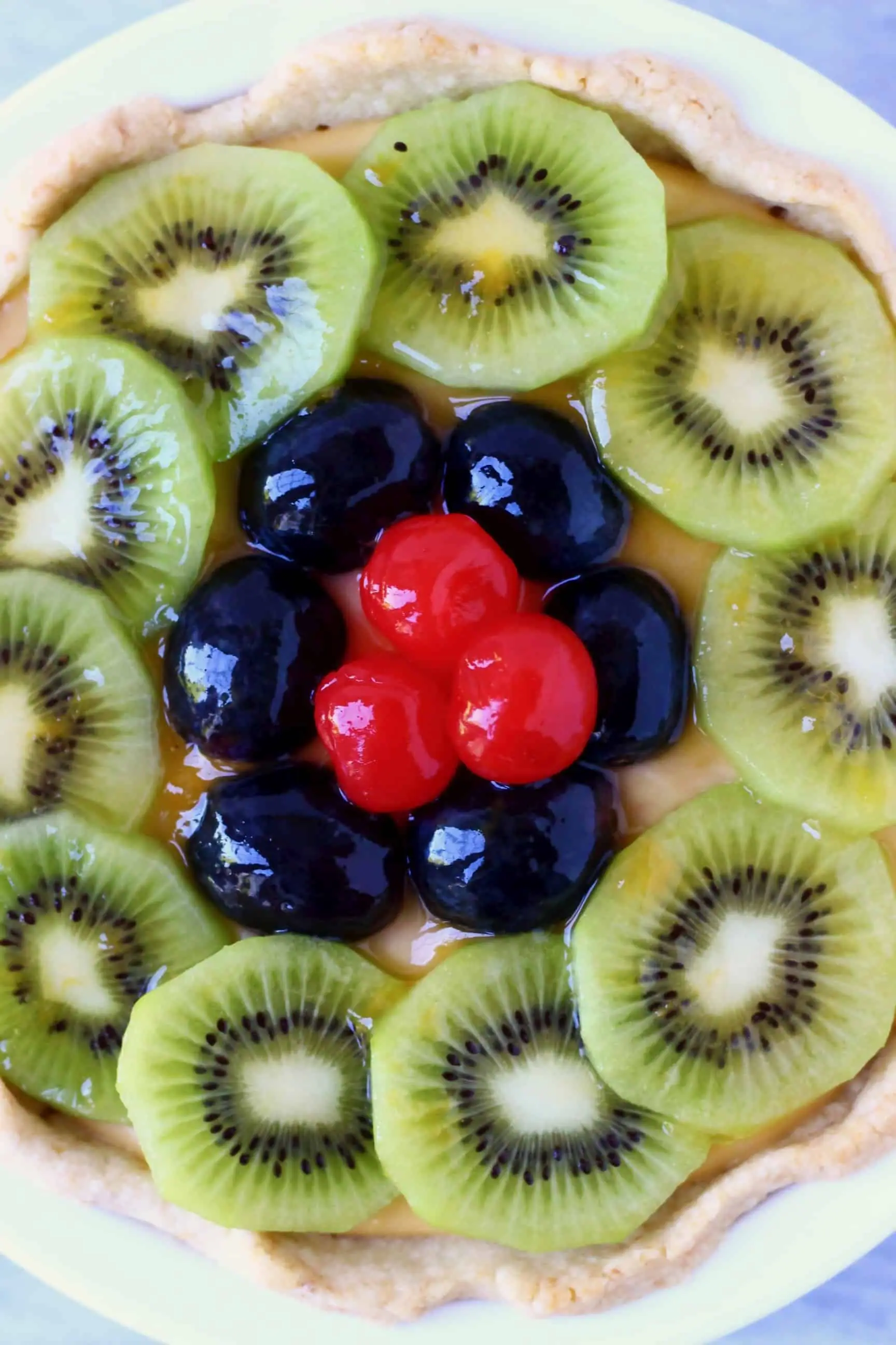 Kiwi slices, black grapes and red cherries on top of a fruit tart in a white pie dish