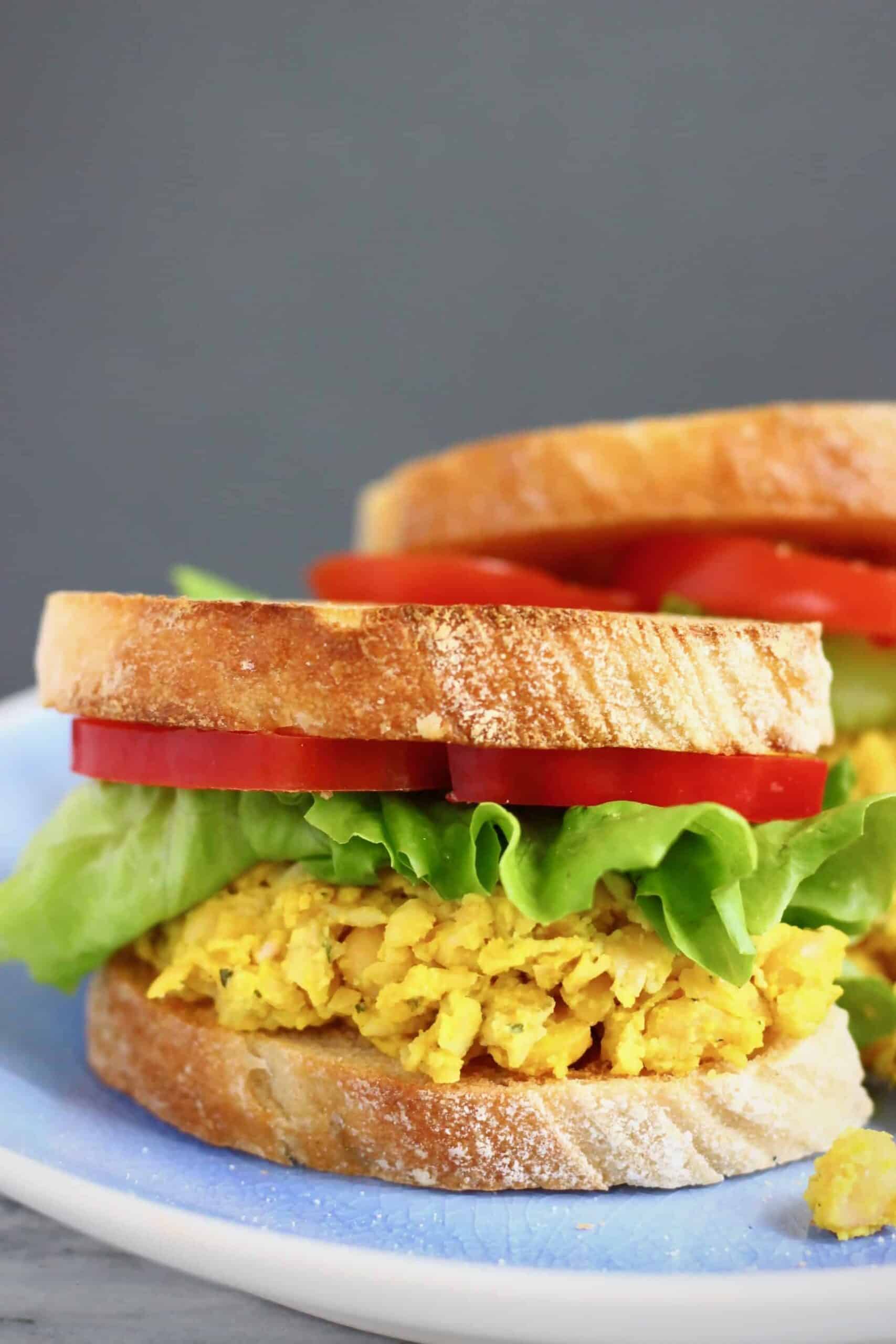 Two sandwiches with curried chickpeas, lettuce and sliced red pepper against a grey background