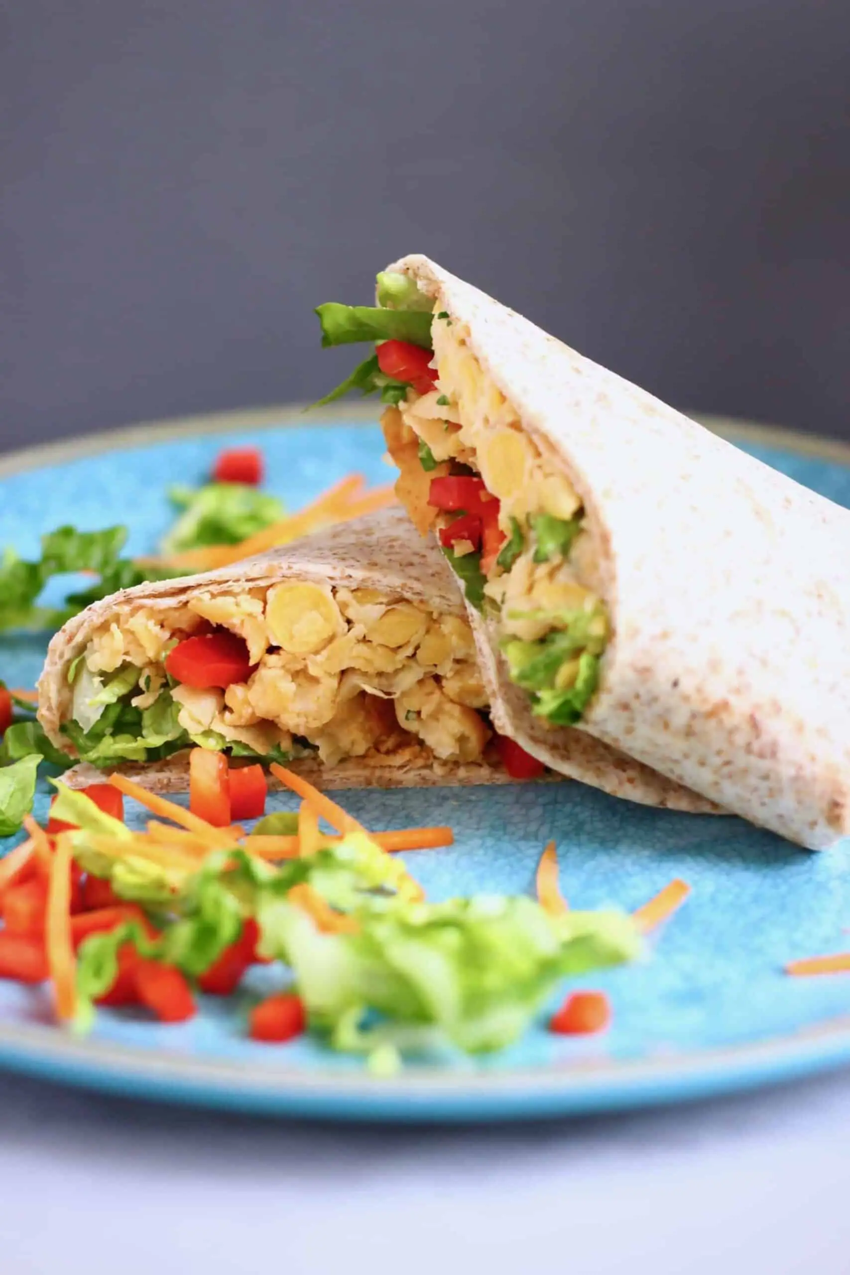 Two wraps filled with chickpeas, lettuce and red pepper on a blue plate against a grey background