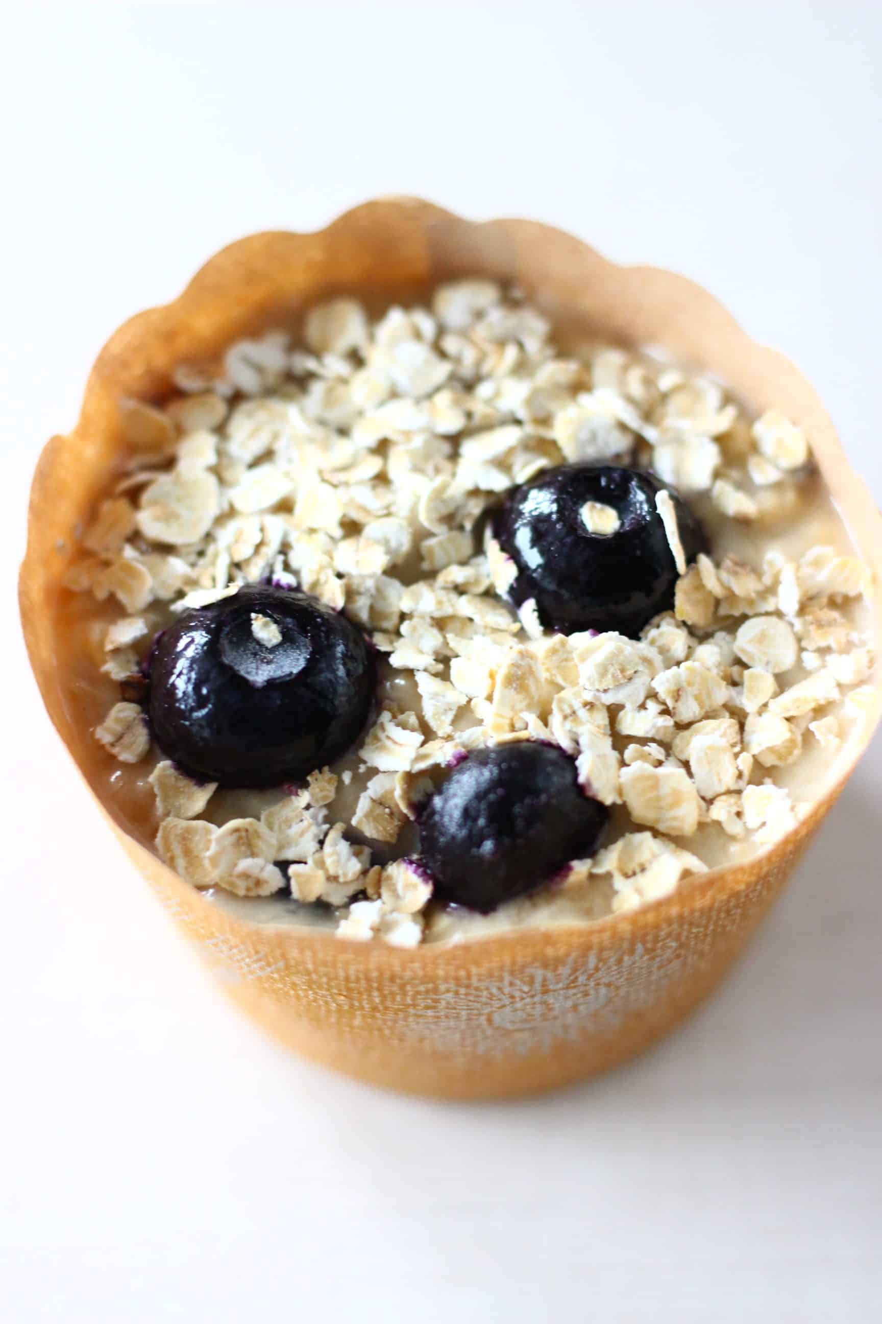 These Gluten-Free Vegan Blueberry Oatmeal Muffins are moist and fluffy, slightly chewy and filled with jammy blueberries! They make a great healthier breakfast, dessert or snack! Dairy-free, egg-free and refined sugar free. #rhiansrecipes #vegan #dairyfree #glutenfree #muffins #dessert A brown muffin case filled with raw gluten-free vegan blueberry oatmeal muffin batter sprinkled with oats