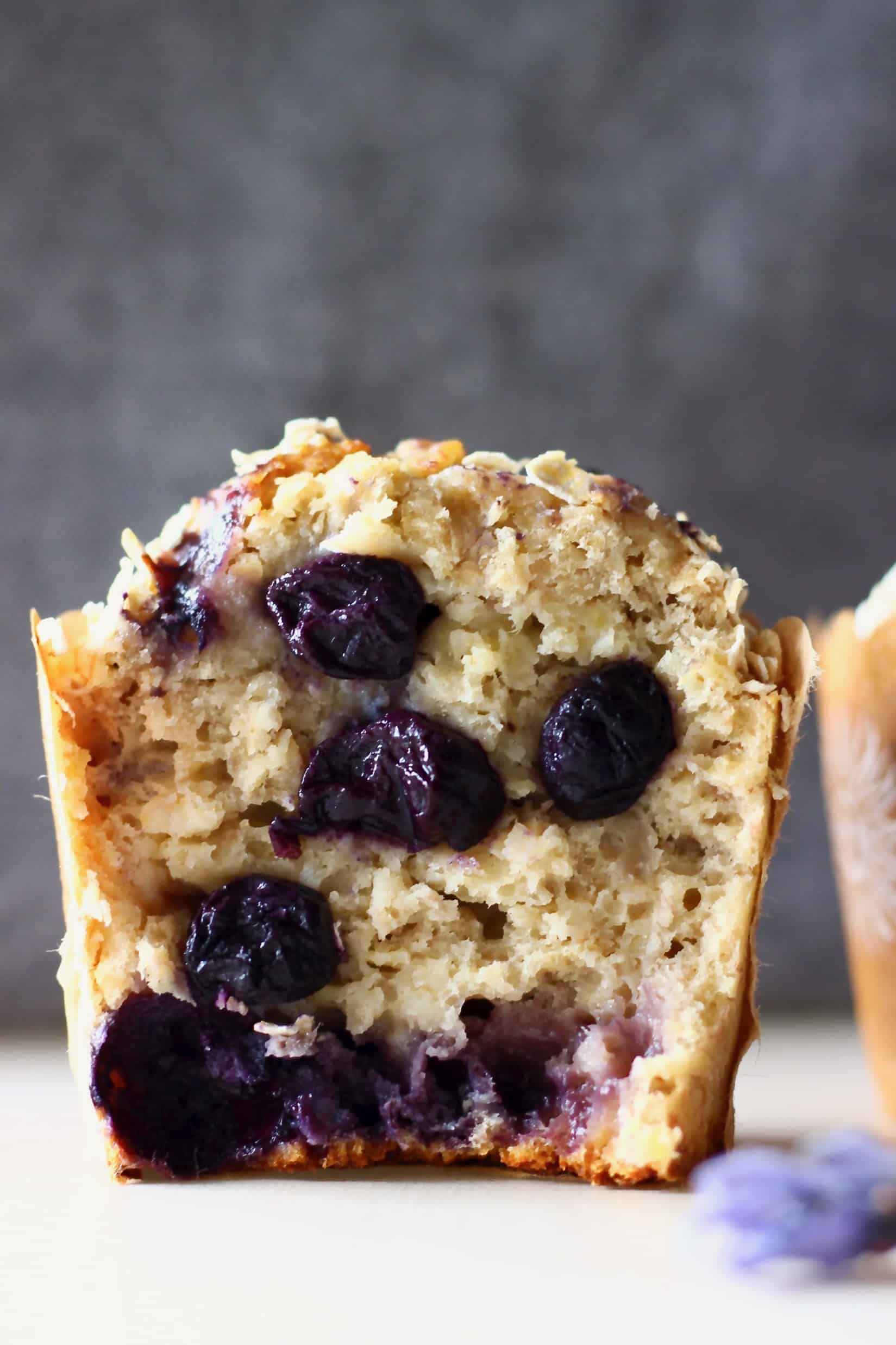 These Gluten-Free Vegan Blueberry Oatmeal Muffins are moist and fluffy, slightly chewy and filled with jammy blueberries! They make a great healthier breakfast, dessert or snack! Dairy-free, egg-free and refined sugar free. #rhiansrecipes #vegan #dairyfree #glutenfree #muffins #dessert A halved gluten-free vegan blueberry oatmeal muffin against a grey background