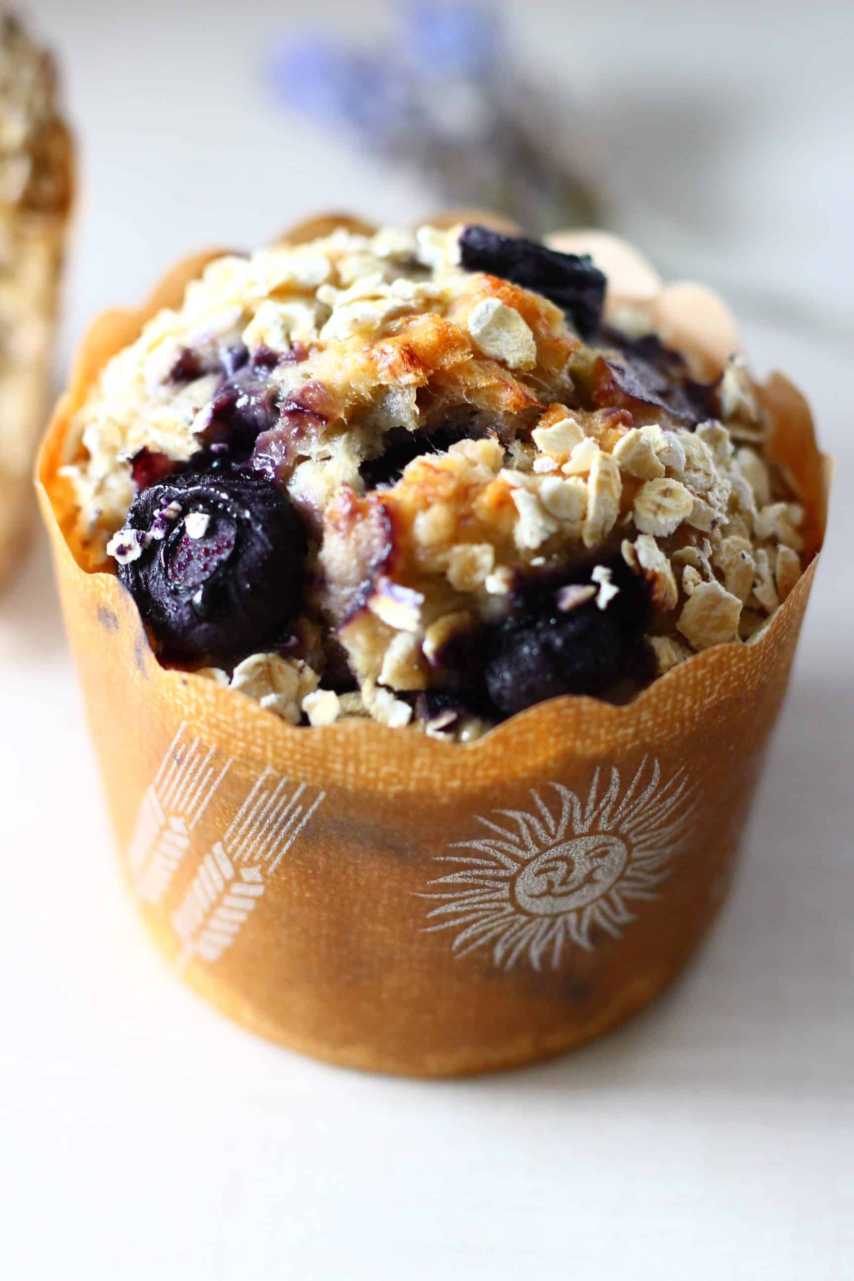A gluten-free vegan blueberry oatmeal muffin topped with oats in a brown muffin case