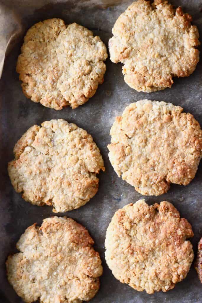 Six golden brown cookies on a baking tray covered in brown baking paper