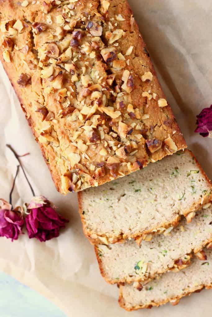 Photo of a loaf of zucchini bread with three slices against a sheet of brown baking paper with two red roses
