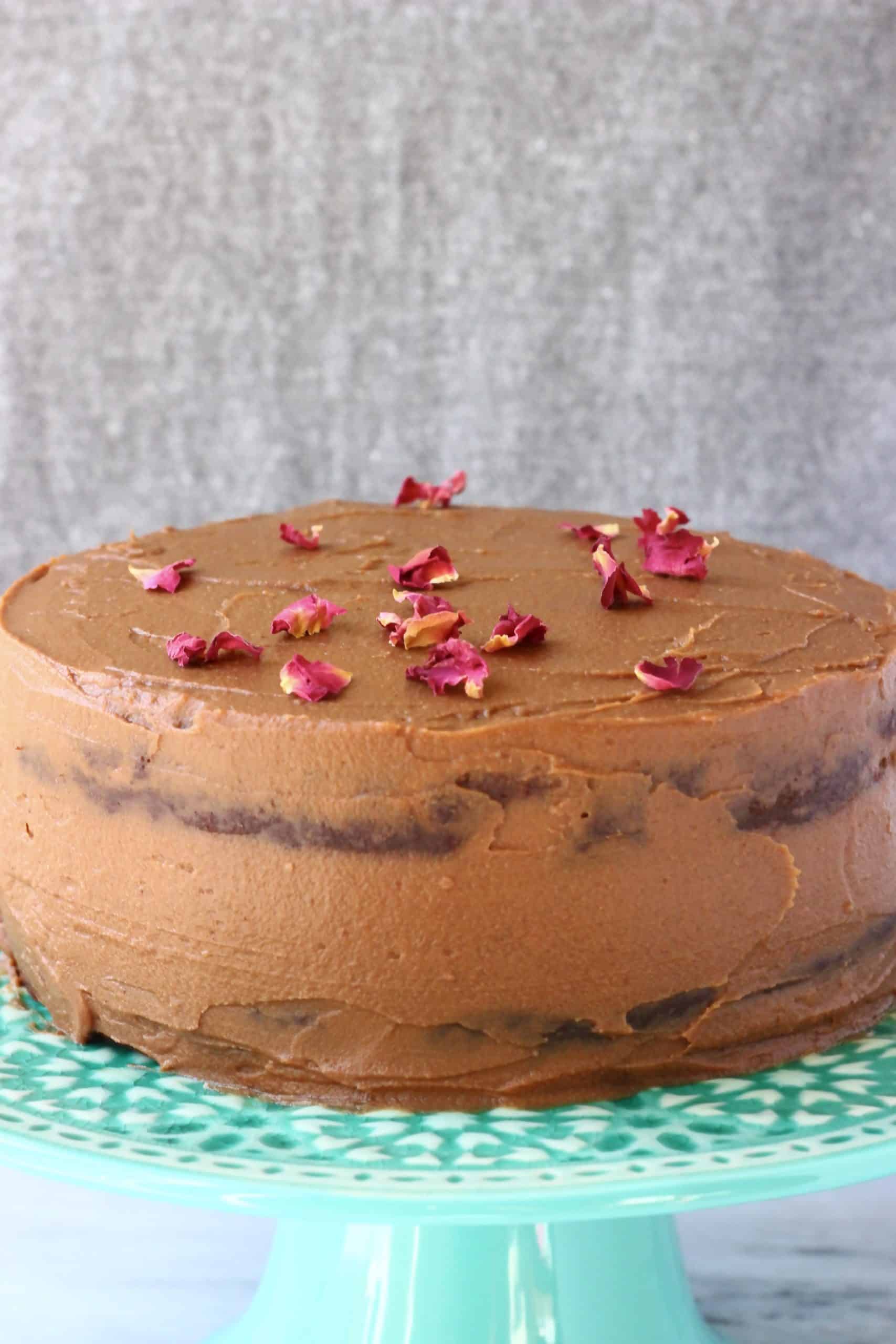 Gluten-free vegan chocolate cake with chocolate frosting sprinkled with rose petals on a cake stand