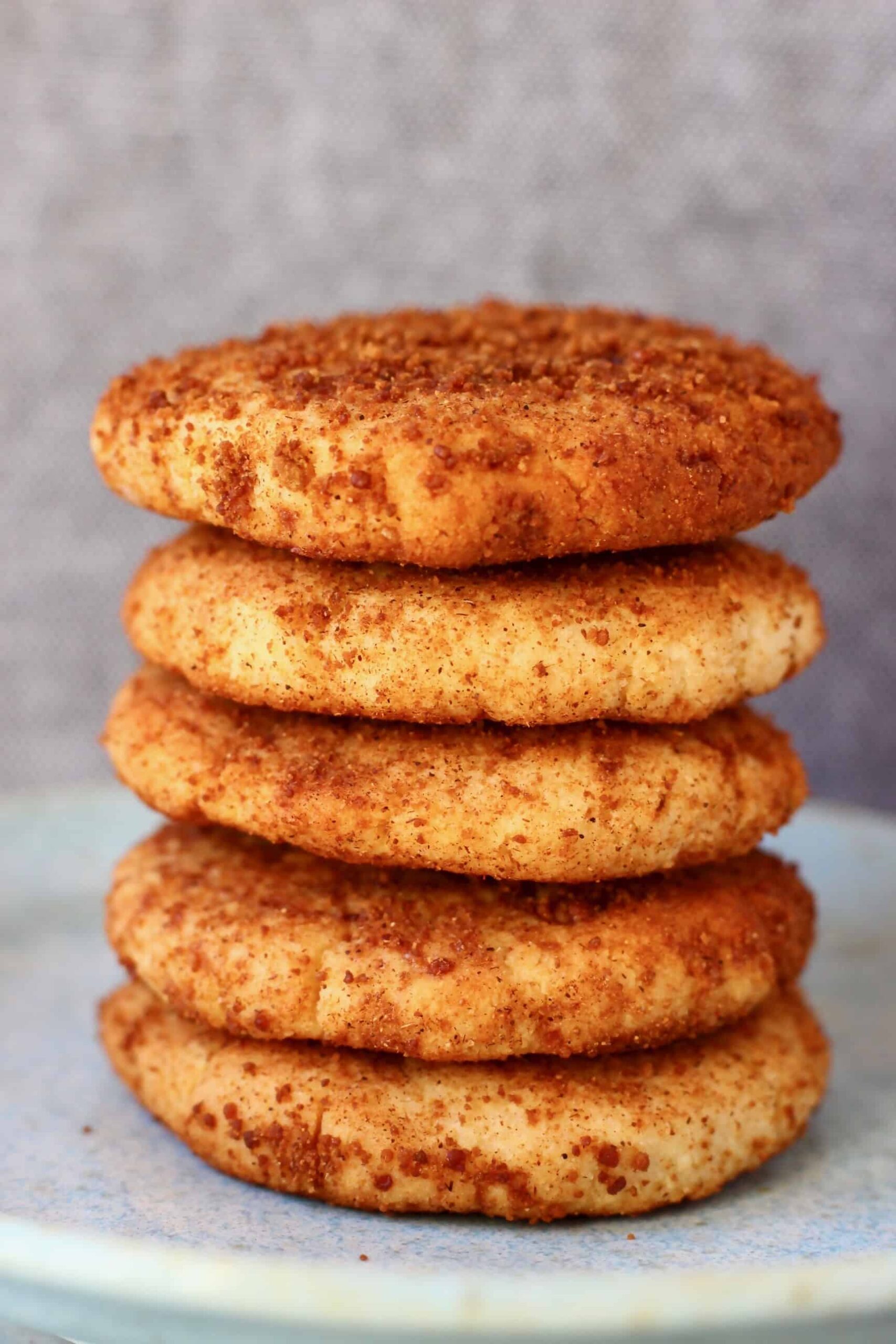 Photo of five cookies coated in brown cinnamon sugar stacked on top of each other on a light blue plate against a grey background
